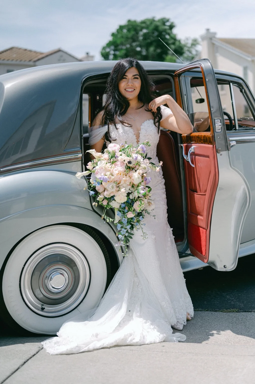 A bride with a cascading bouquet beside the Bentley's red leather door