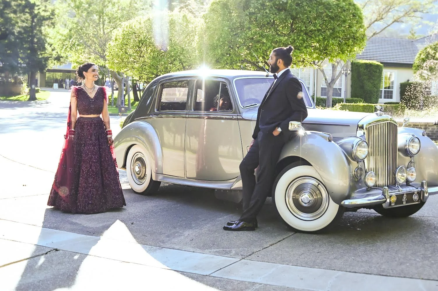 A wedding couple in formal attire beside the Bentley in sunlight