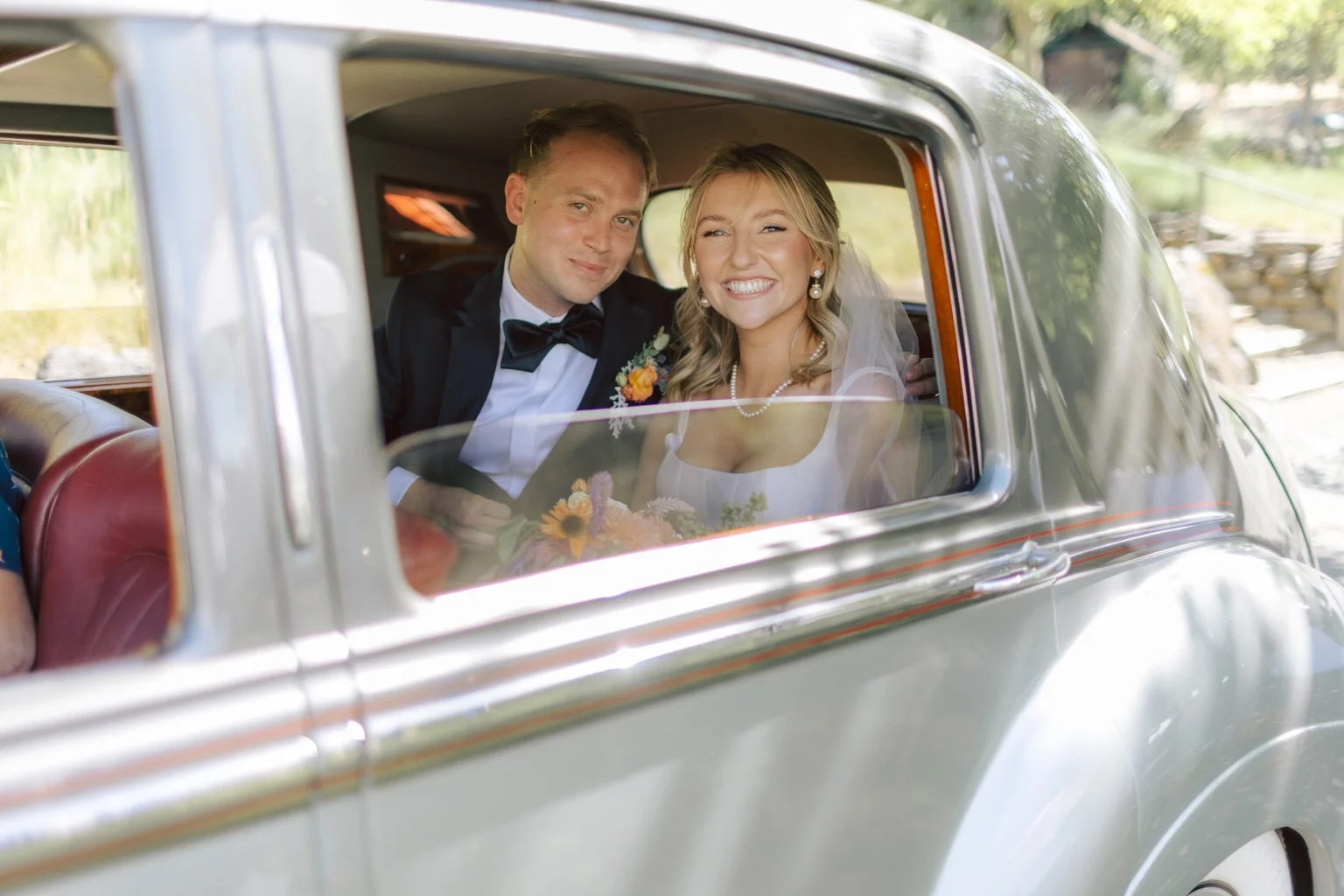 A smiling wedding couple through the Bentley's rear window